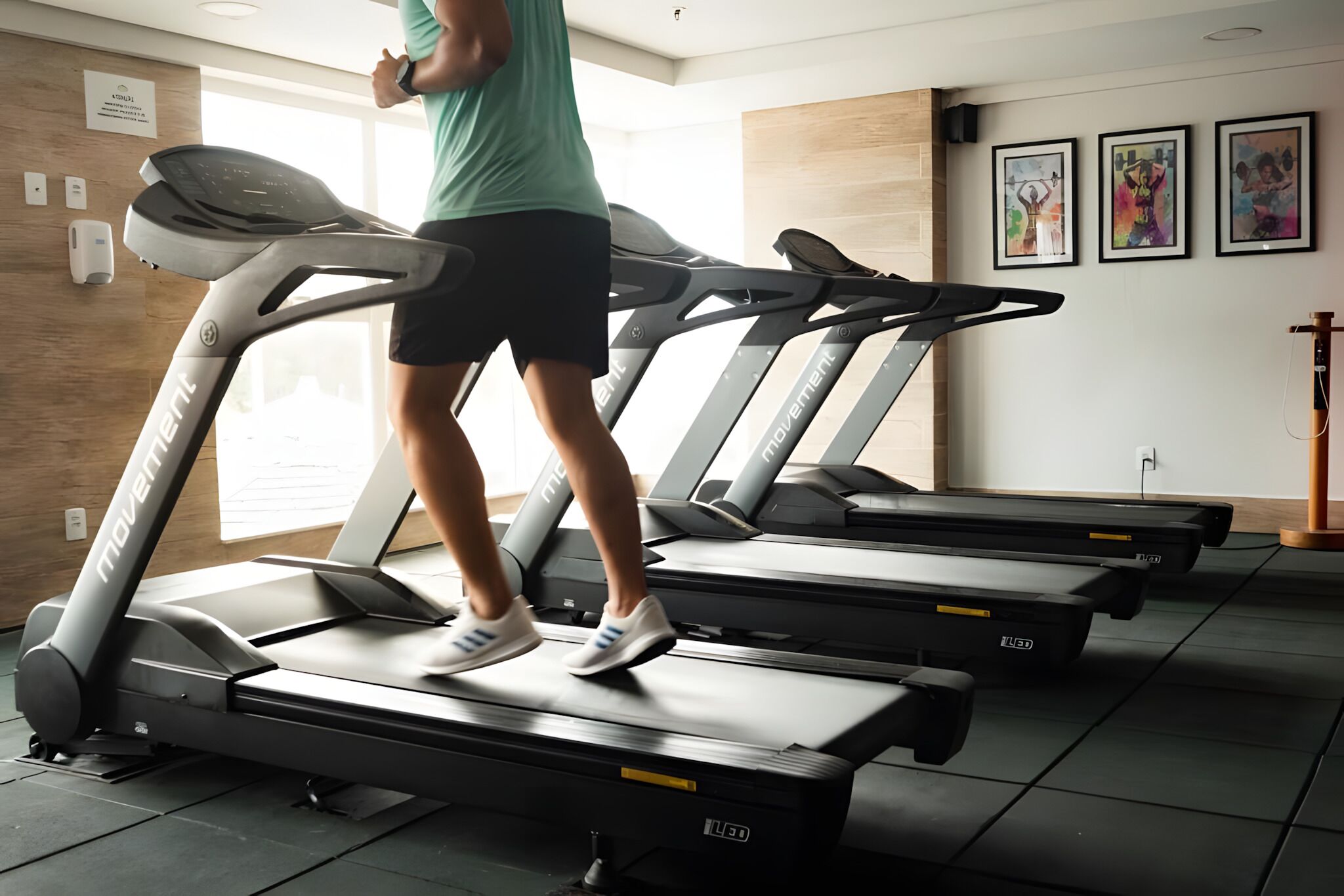 Un gimnasio con cintas de correr, dispensador de gel hidroalcohólico en la pared y obras de arte enmarcadas.