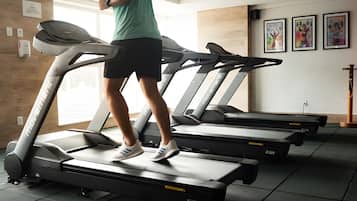 Un gimnasio con cintas de correr, dispensador de gel hidroalcohólico en la pared y obras de arte enmarcadas.