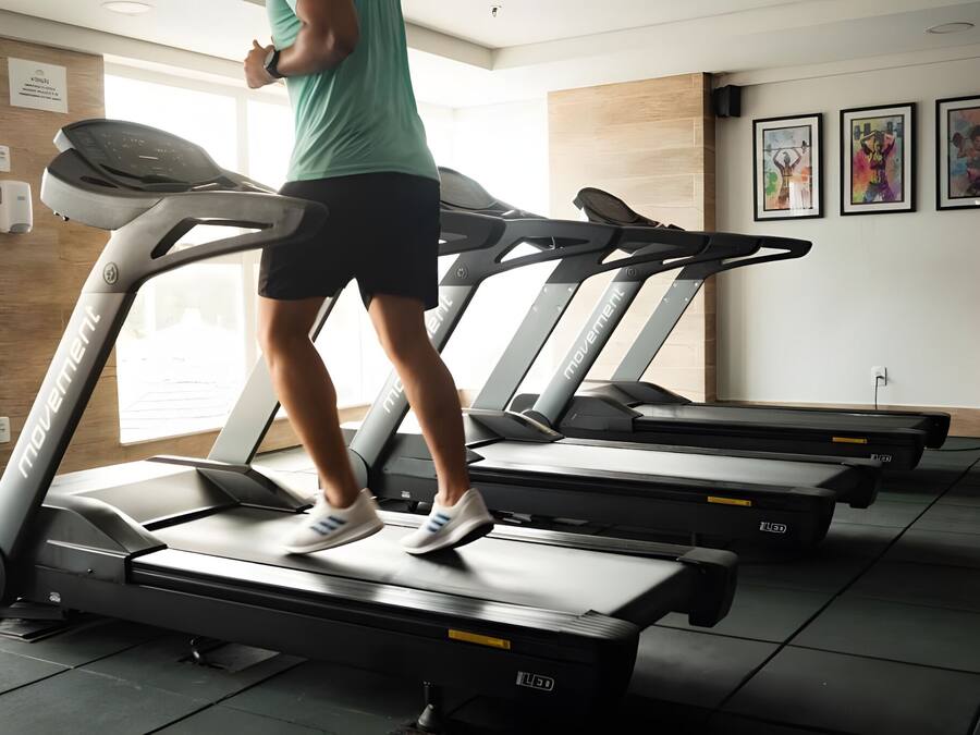 Un gimnasio con cintas de correr, dispensador de gel hidroalcohólico en la pared y obras de arte enmarcadas.