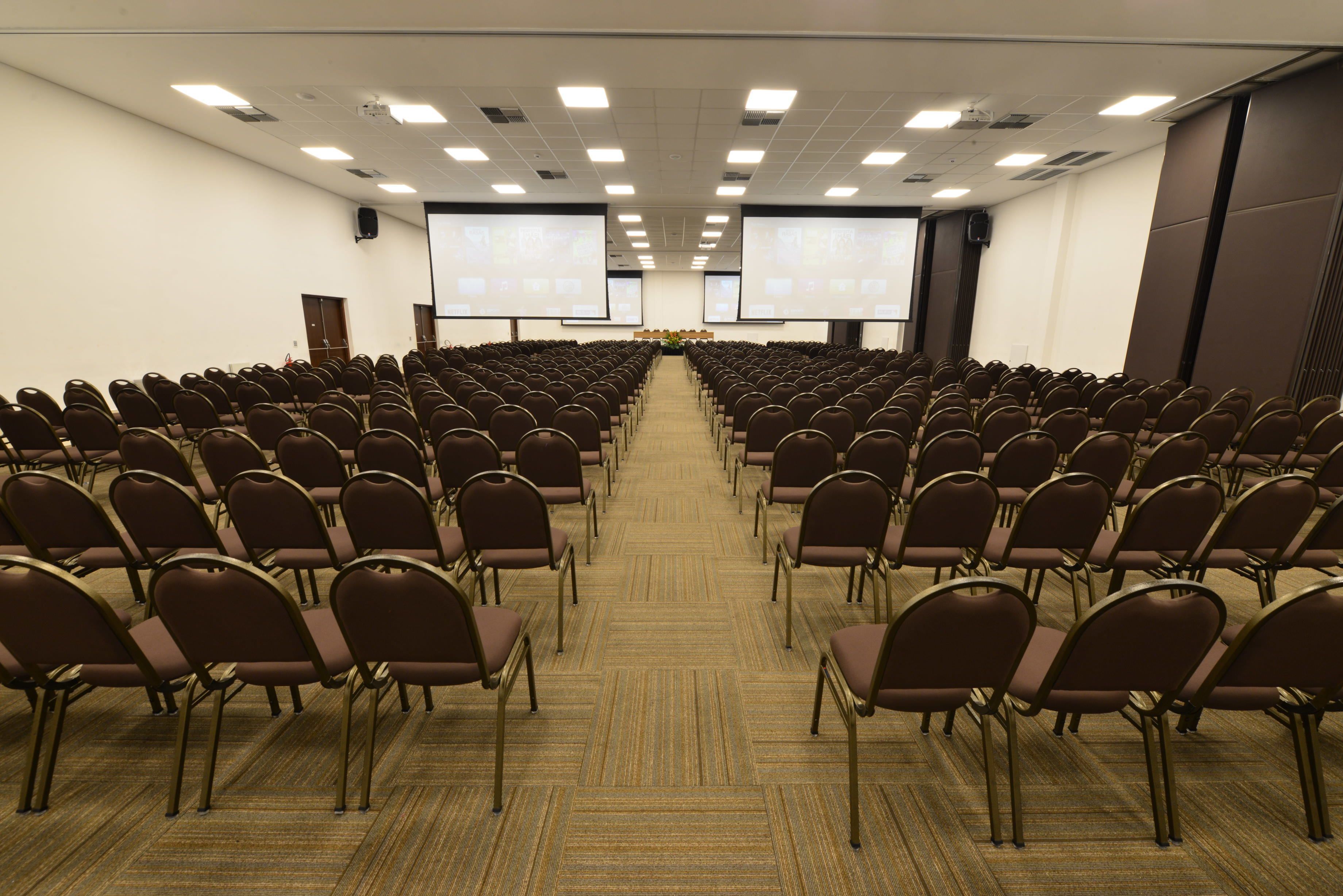 A conference room with rows of chairs facing a large screen at the front.