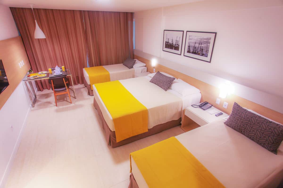 A hotel room with two beds, a desk, and a chair. There are two bedside tables with lamps and a small table with a chair and a plate of fruit.