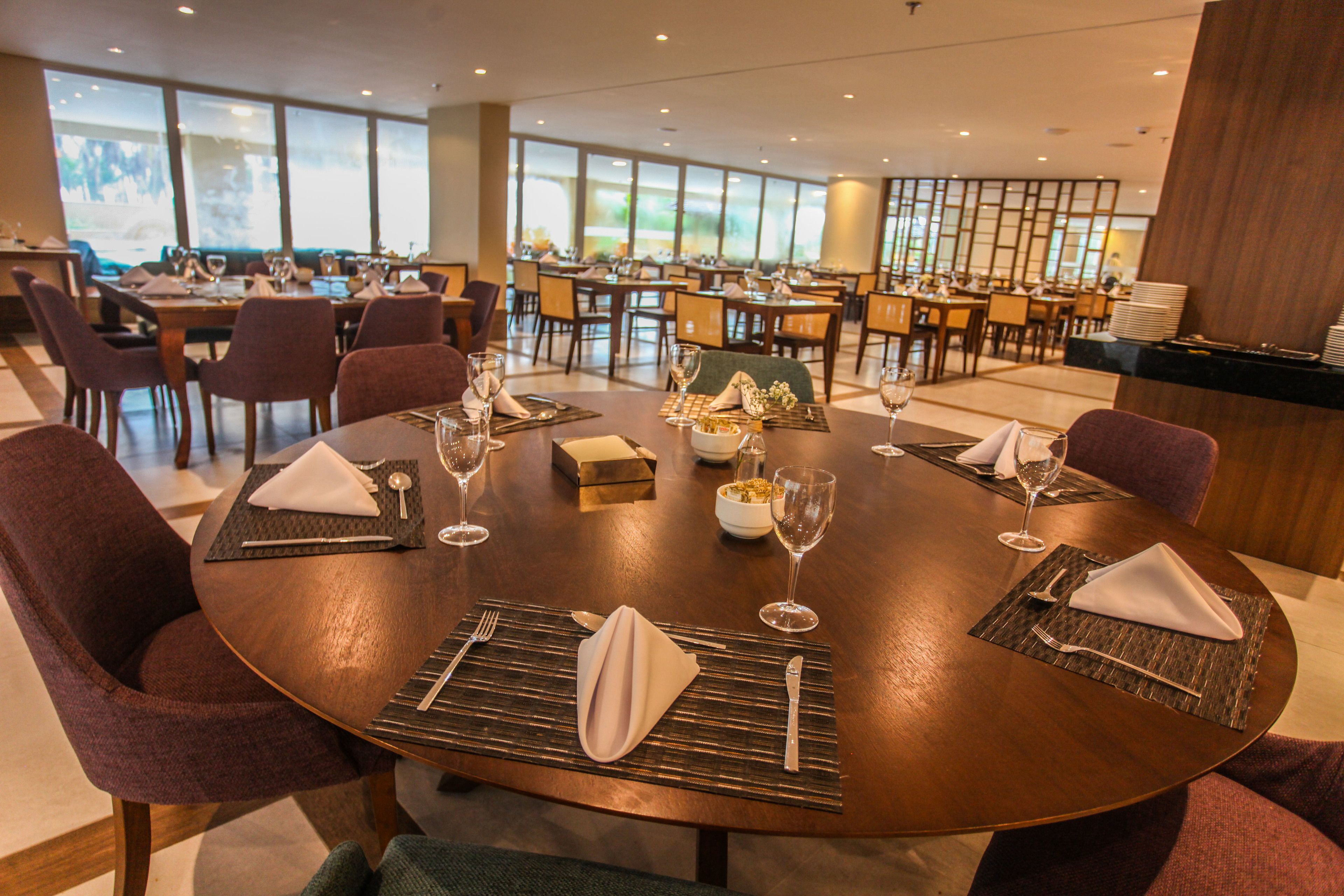 Un comedor con mesas redondas dispuestas para cuatro comensales, cada una con servilleta, cubiertos y cristalería.