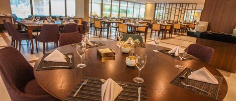 Un comedor con mesas redondas dispuestas para cuatro comensales, cada una con servilleta, cubiertos y cristalería.