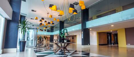 A spacious lobby with a checkered floor, modern pendant lighting, and a central table with chairs.