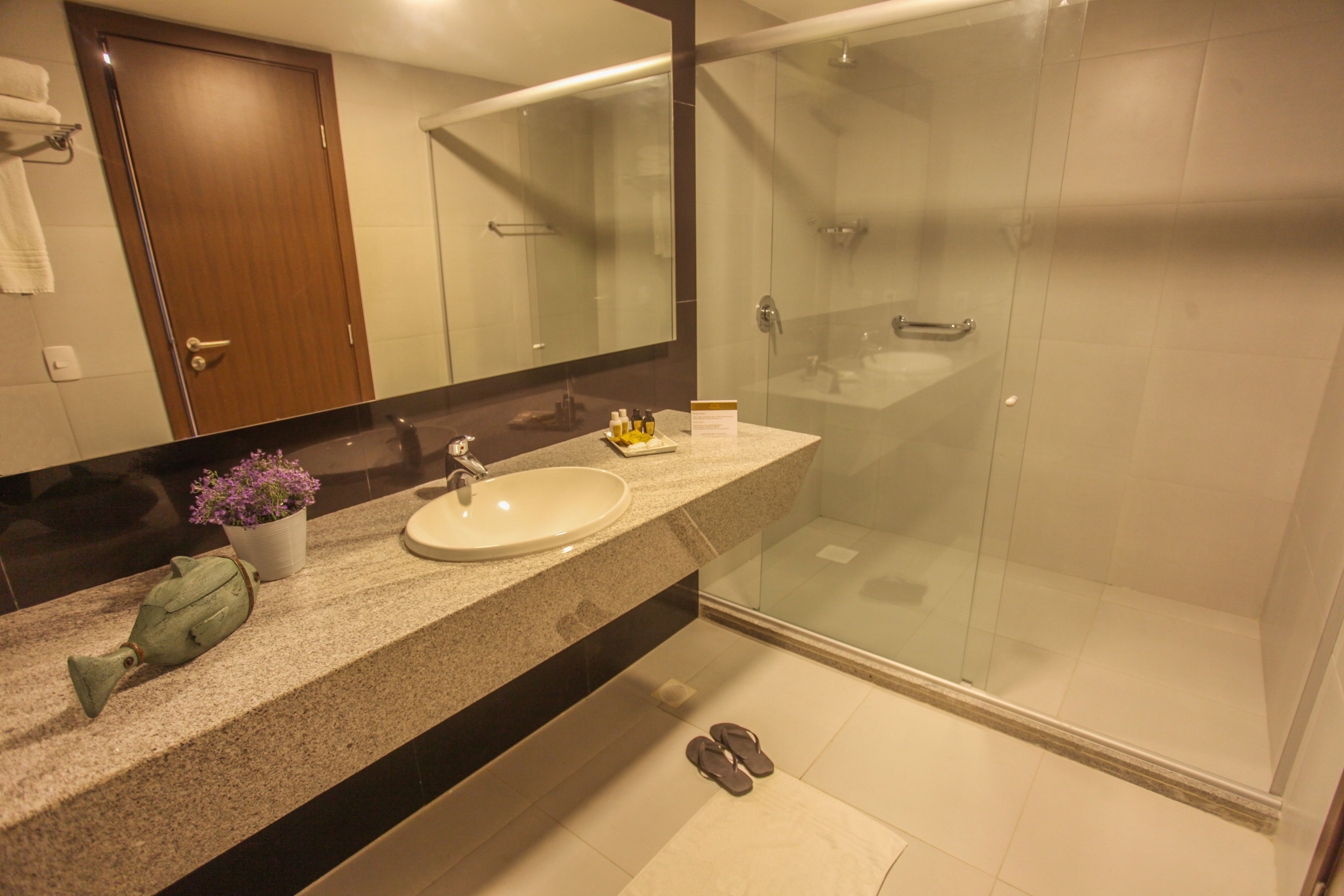 Une salle de bain avec un lavabo, un miroir, une douche et une paire de chaussures sur le sol.