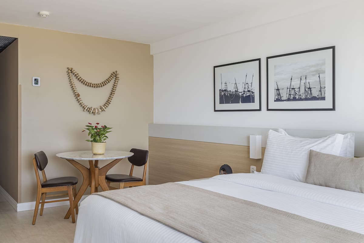 A hotel room with a bed, a round table with chairs, a potted plant, and two framed pictures on the wall.