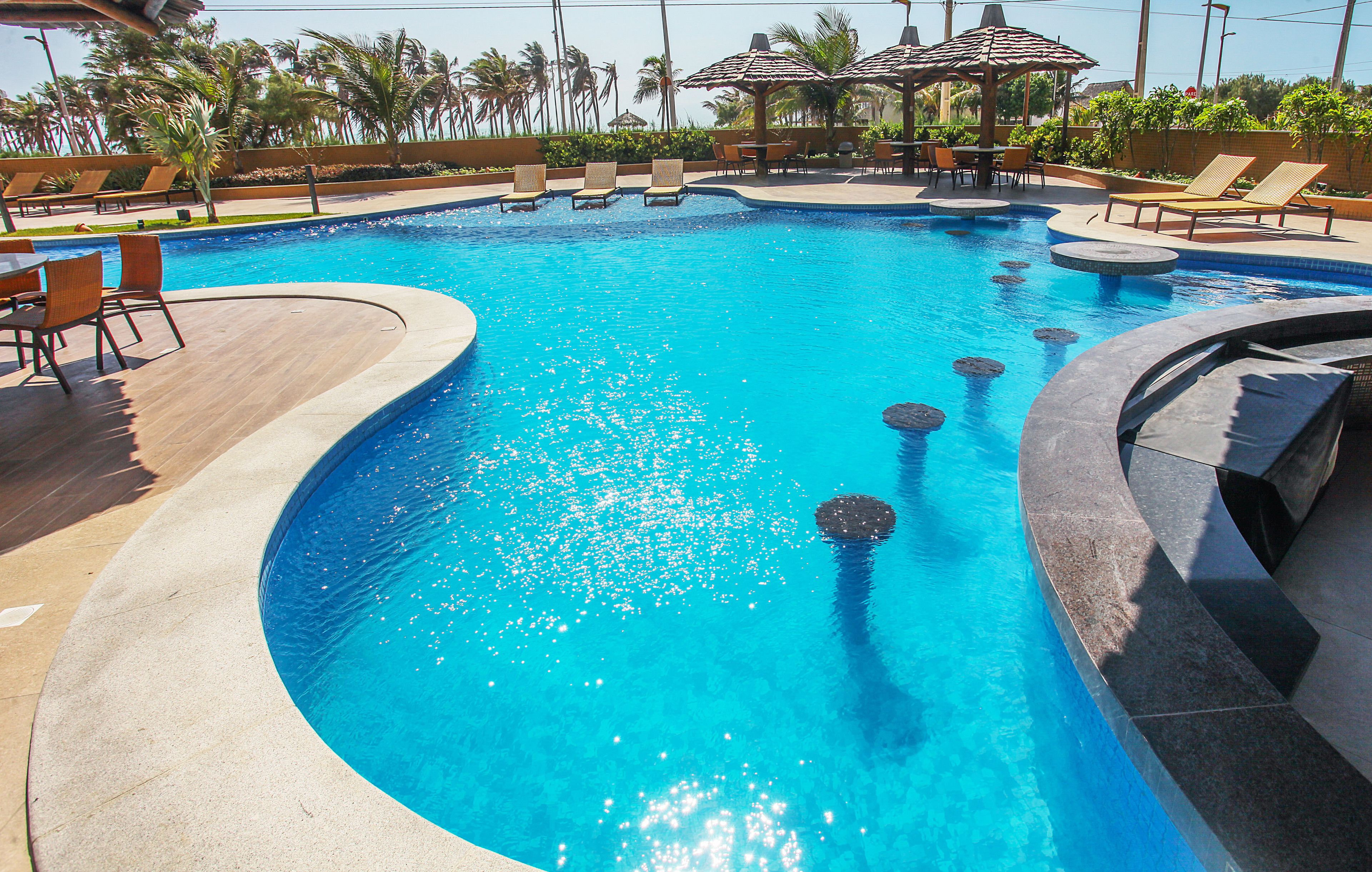 A swimming pool with lounge chairs and umbrellas, surrounded by palm trees and a clear sky.