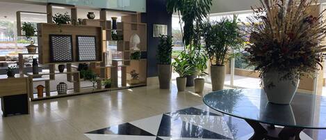 Un moderno vestíbulo de hotel con piso de patrón geométrico, una mesa de centro de vidrio y diversas plantas en macetas.