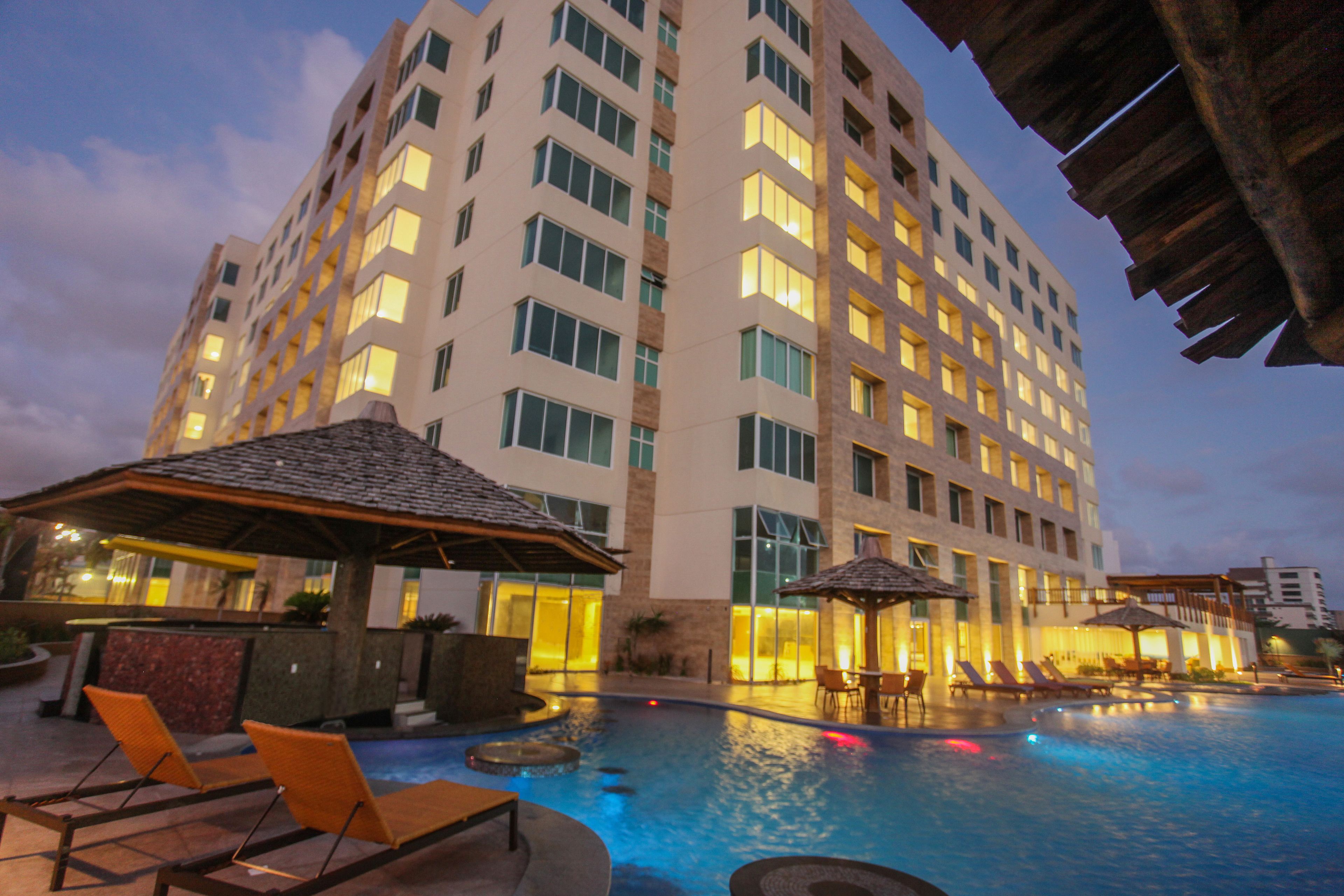 A hotel with a swimming pool, lounge chairs, and a bar area.