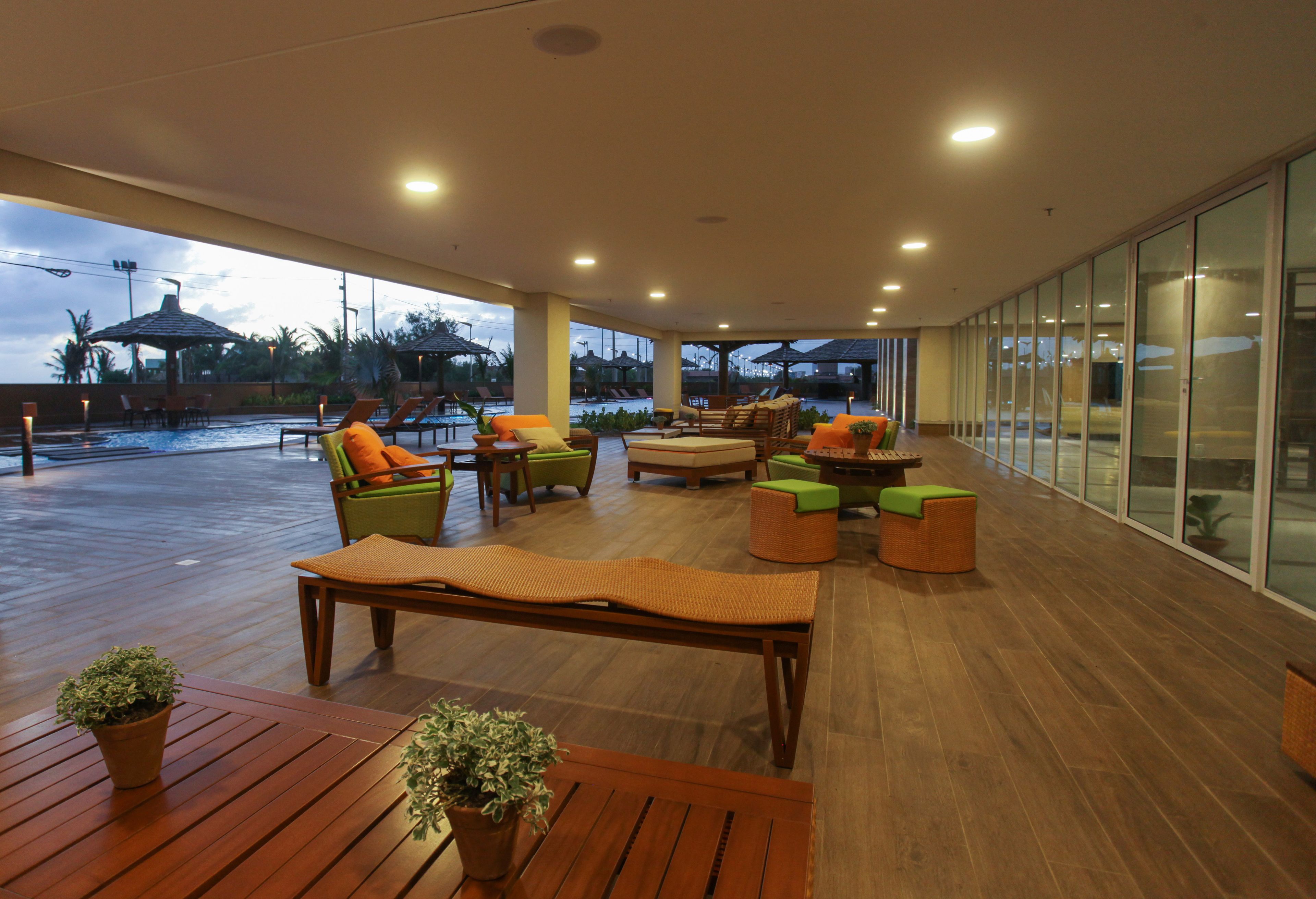 A spacious outdoor lounge area with wooden flooring, comfortable seating, and a view of the pool.
