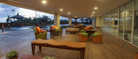 A spacious outdoor lounge area with wooden flooring, comfortable seating, and a view of the pool.