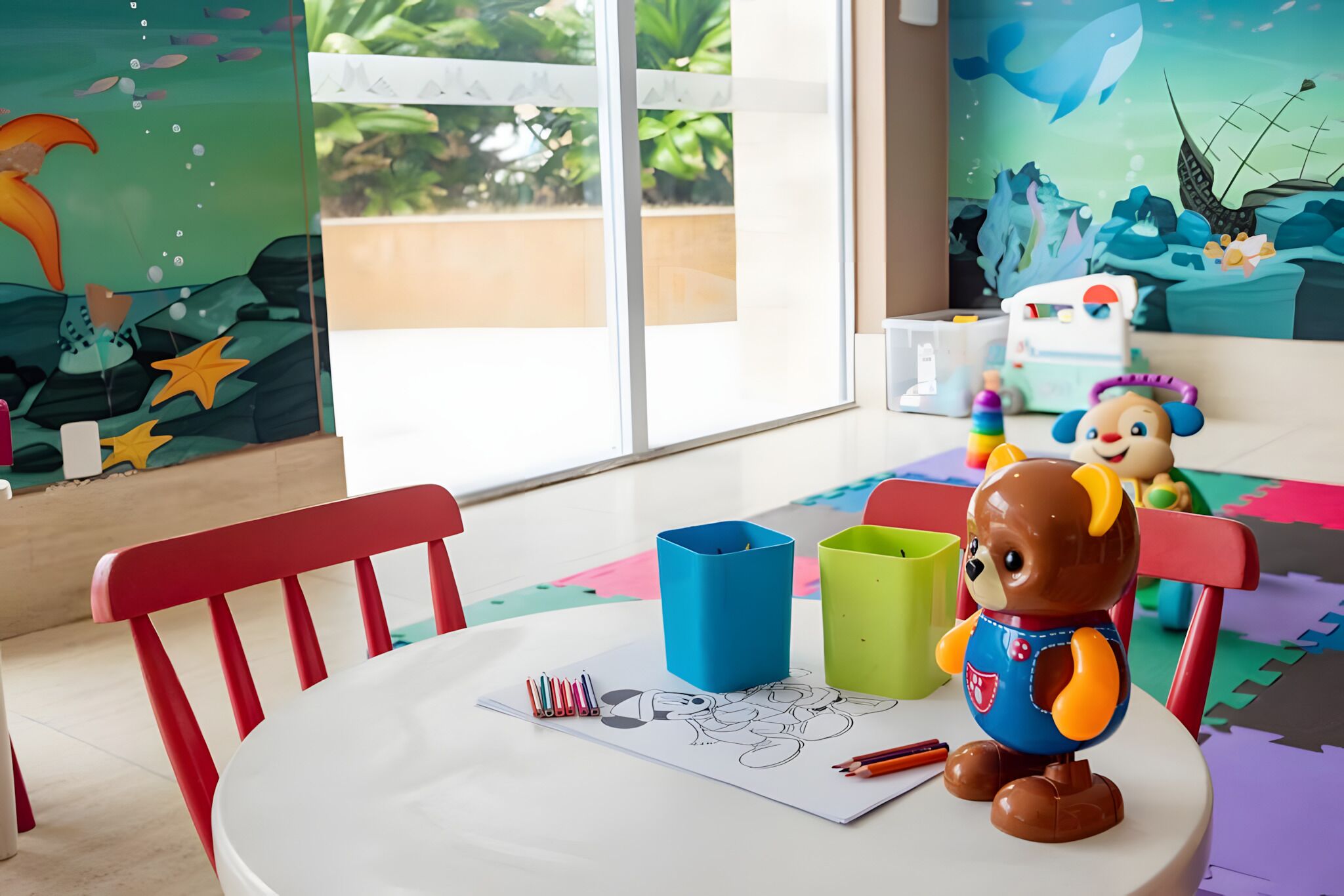 Espaço infantil com mesa, cadeiras e brinquedos.
