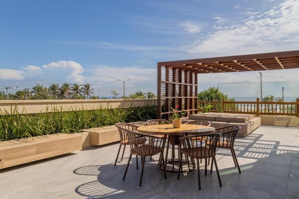 Une terrasse extérieure avec une table ronde et des chaises, une pergola et une vue sur l’océan.