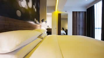 A modern hotel room with a large bed, a wooden headboard, a mirror, and a view of the city through large windows.
