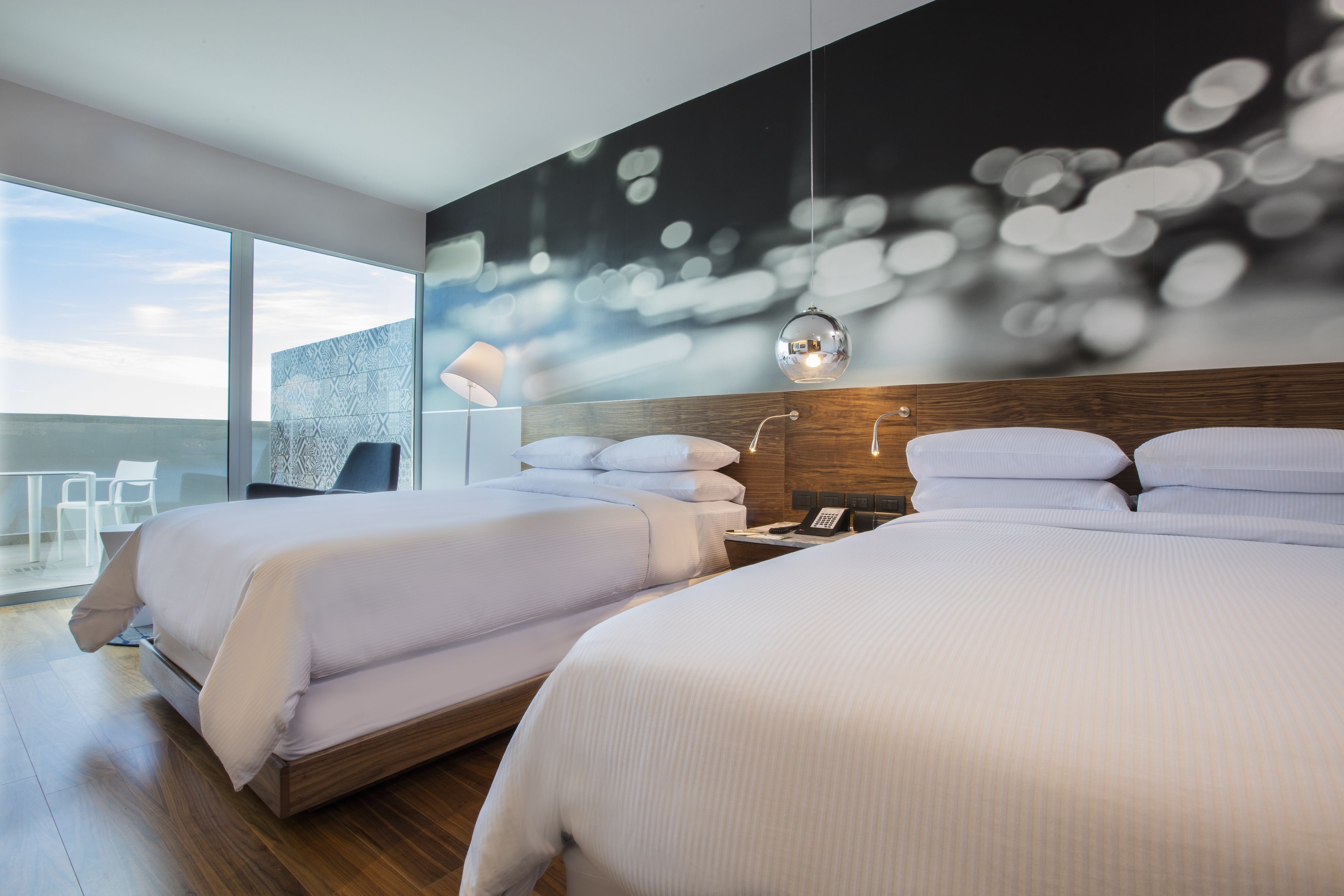 A modern hotel room with two beds, a large window, and a cityscape view.