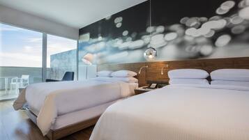 A modern hotel room with two beds, a large window, and a cityscape view.