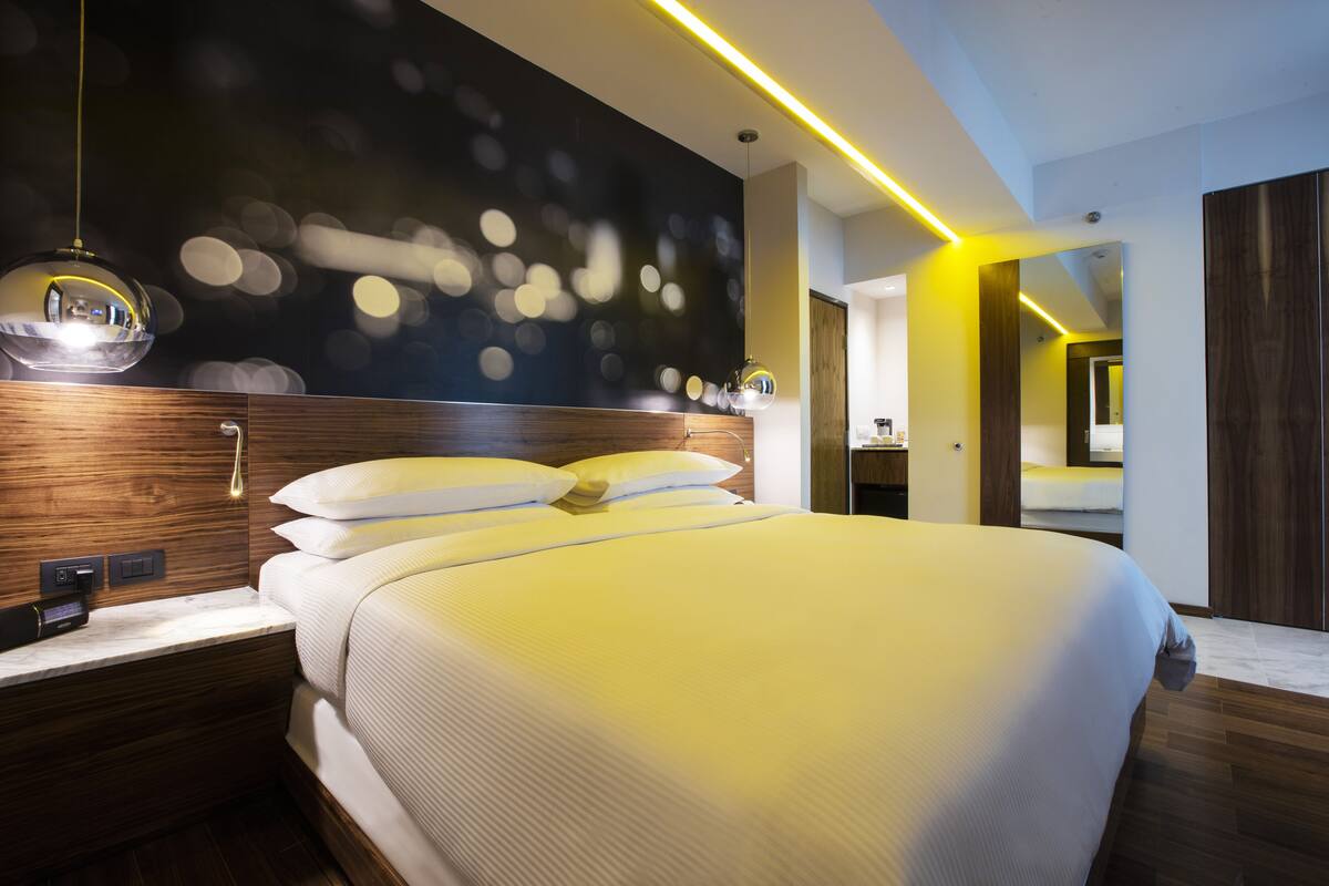 Una habitación de hotel moderna con una cama grande, cabecera de madera y una pared oscura con luces bokeh.