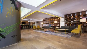 A spacious lobby with a high ceiling, a central seating area, and a large bookshelf. - Krystal Urban Guadalajara (Guadalajara)