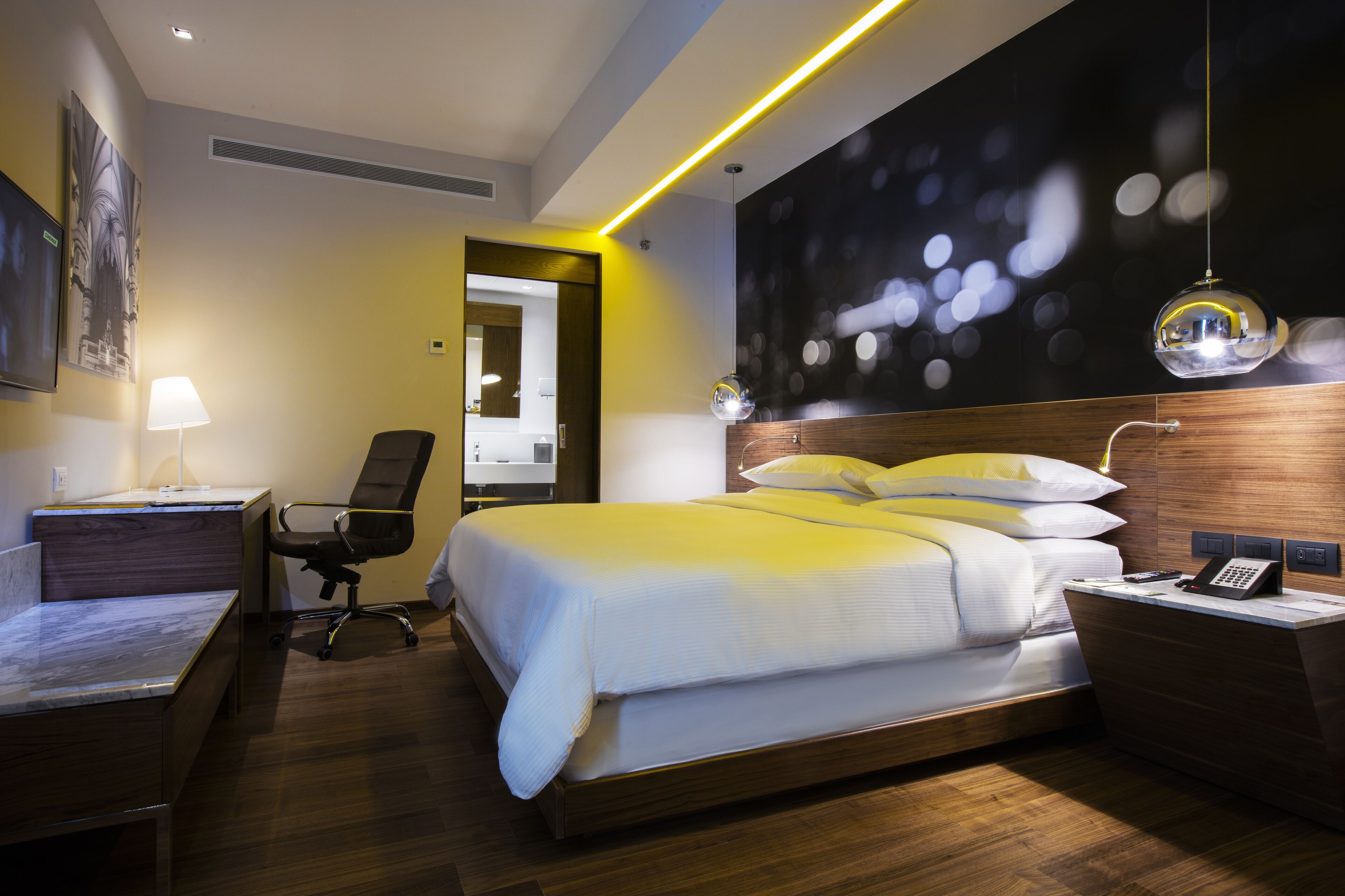 Una habitación de hotel moderna con una cama grande, un escritorio, una silla y una lámpara de escritorio.