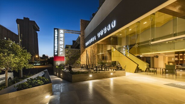 A modern hotel entrance with a glass facade, outdoor seating area, and a staircase leading to the lobby. - Krystal Urban Guadalajara (Guadalajara)