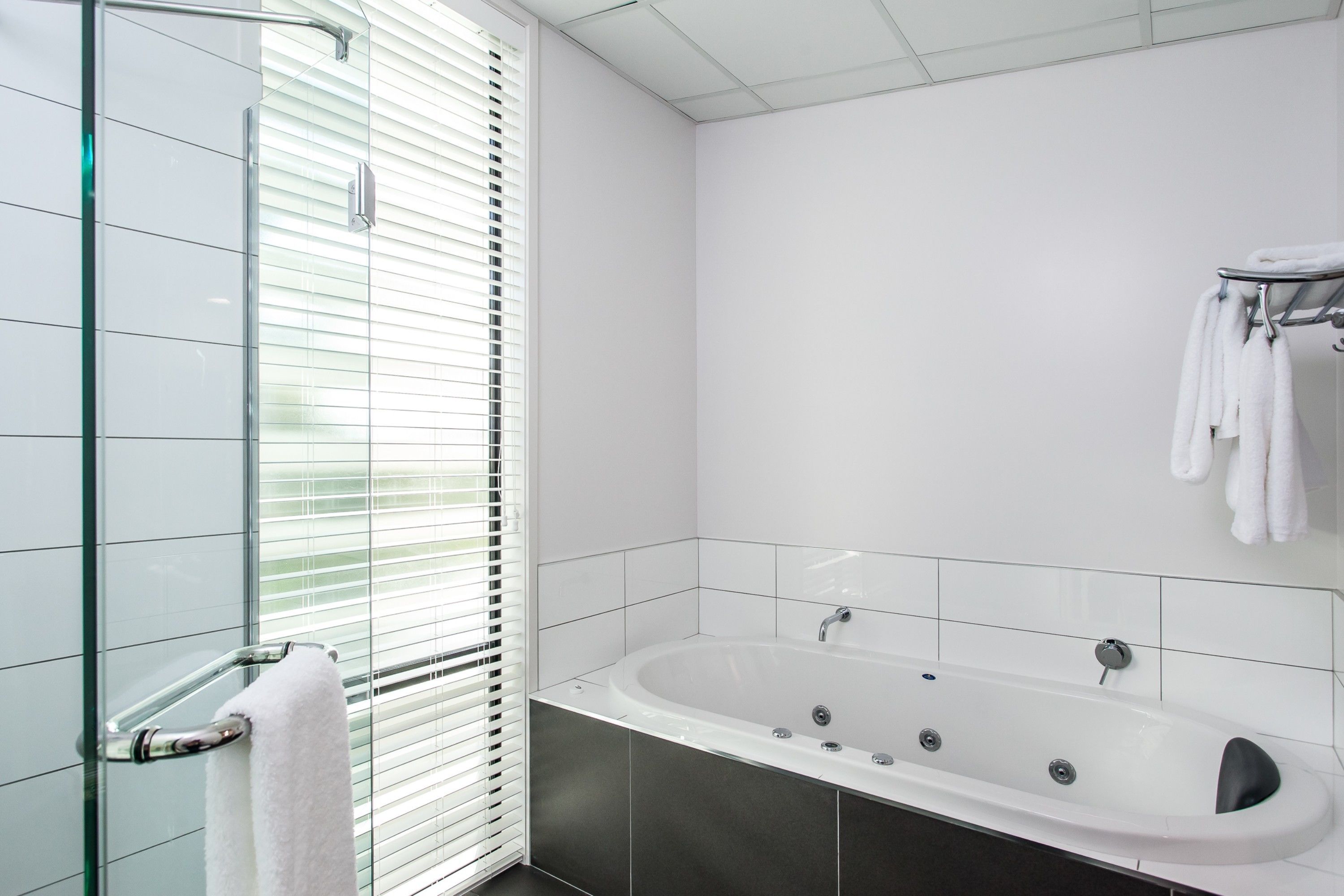Un baño moderno con cabina de ducha de vidrio, una bañera blanca y un perchero con toallas.
