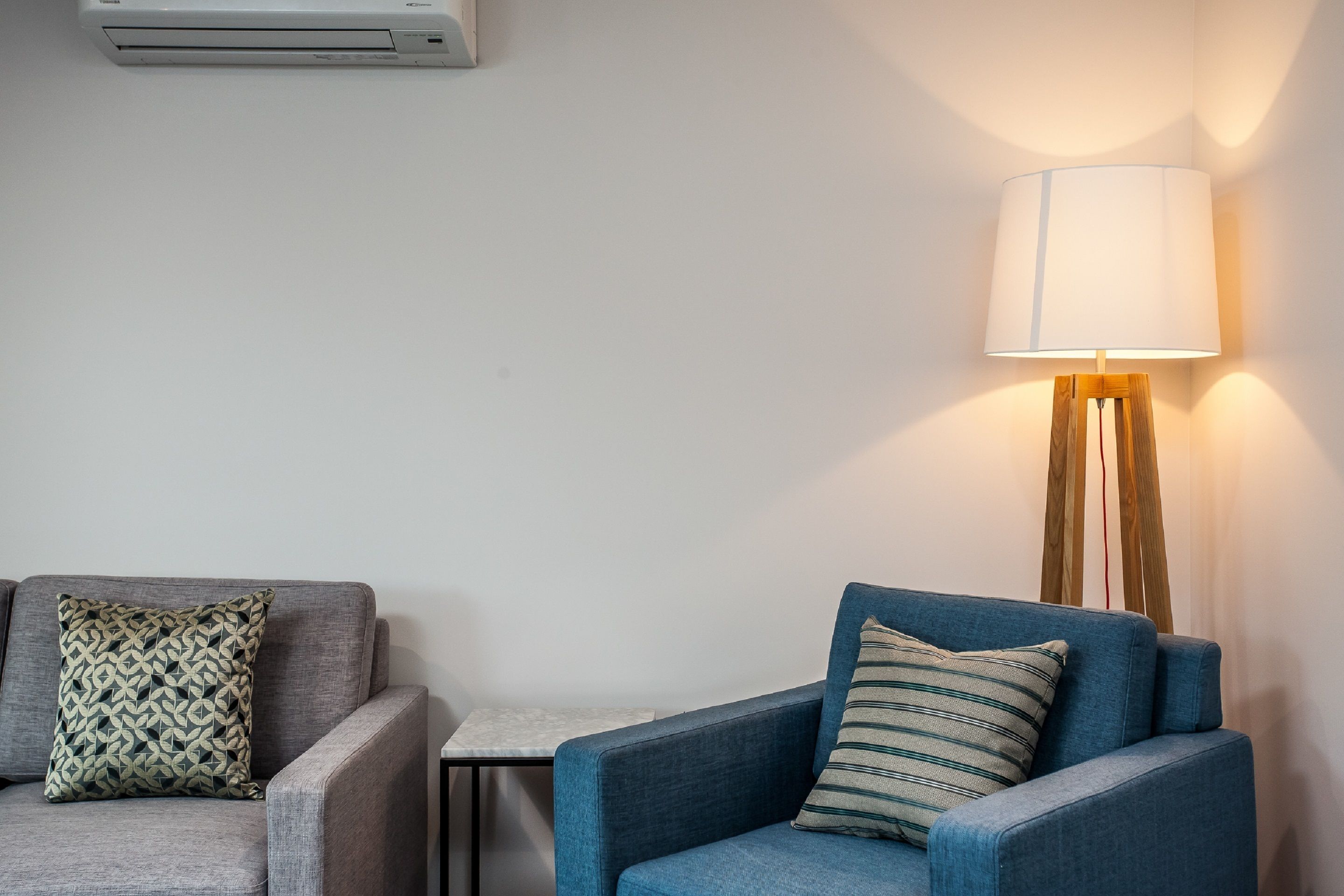 Una sala de estar moderna con un sofá gris, un sillón azul, un cojín estampado, una mesita auxiliar y una lámpara de pie.