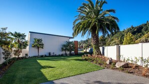 A modern building with a flat roof, surrounded by a well-maintained lawn and palm trees. - One88 On Commerce (Whakatane)