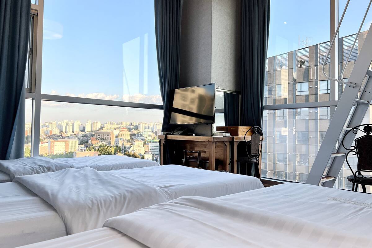 A hotel room with two beds, a TV, and a city view.