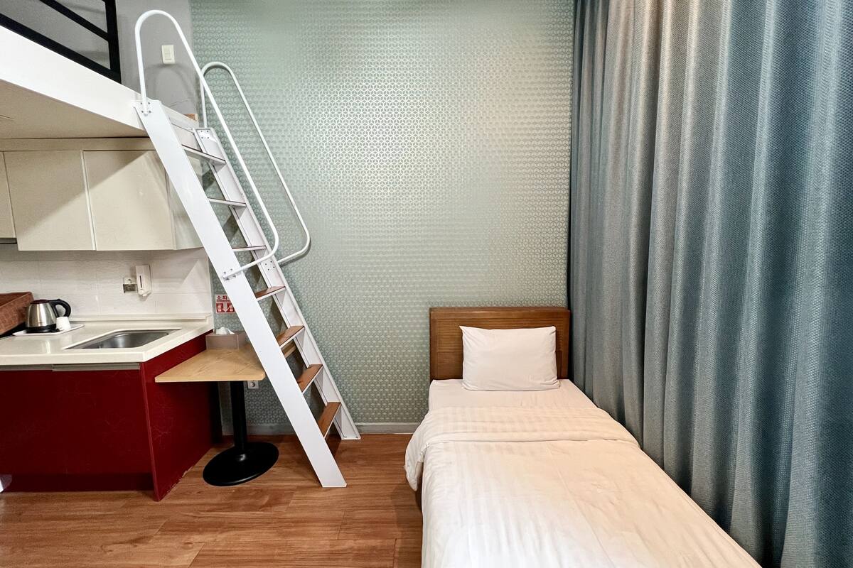 A compact hotel room with a bunk bed, a kitchenette, and a single bed.