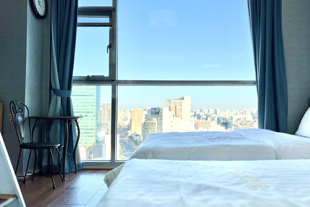 A bedroom with a large window, a bed, a chair, and a clock on the wall.