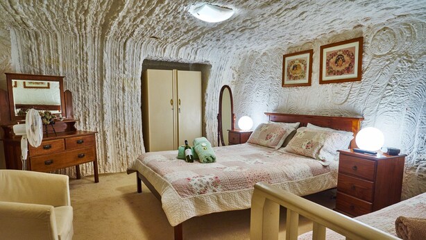 A bedroom with a bed, dresser, mirror, and two wall-mounted lights. - Underground Bed and Breakfast (Coober Pedy)