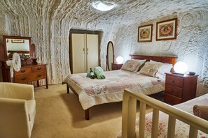 A bedroom with a bed, dresser, mirror, and two wall-mounted lights. - Underground Bed and Breakfast (Coober Pedy)