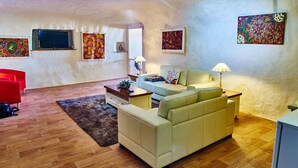 A cozy living room with a sofa, a red chair, a coffee table, and a TV mounted on the wall. - Underground Bed and Breakfast (Coober Pedy)