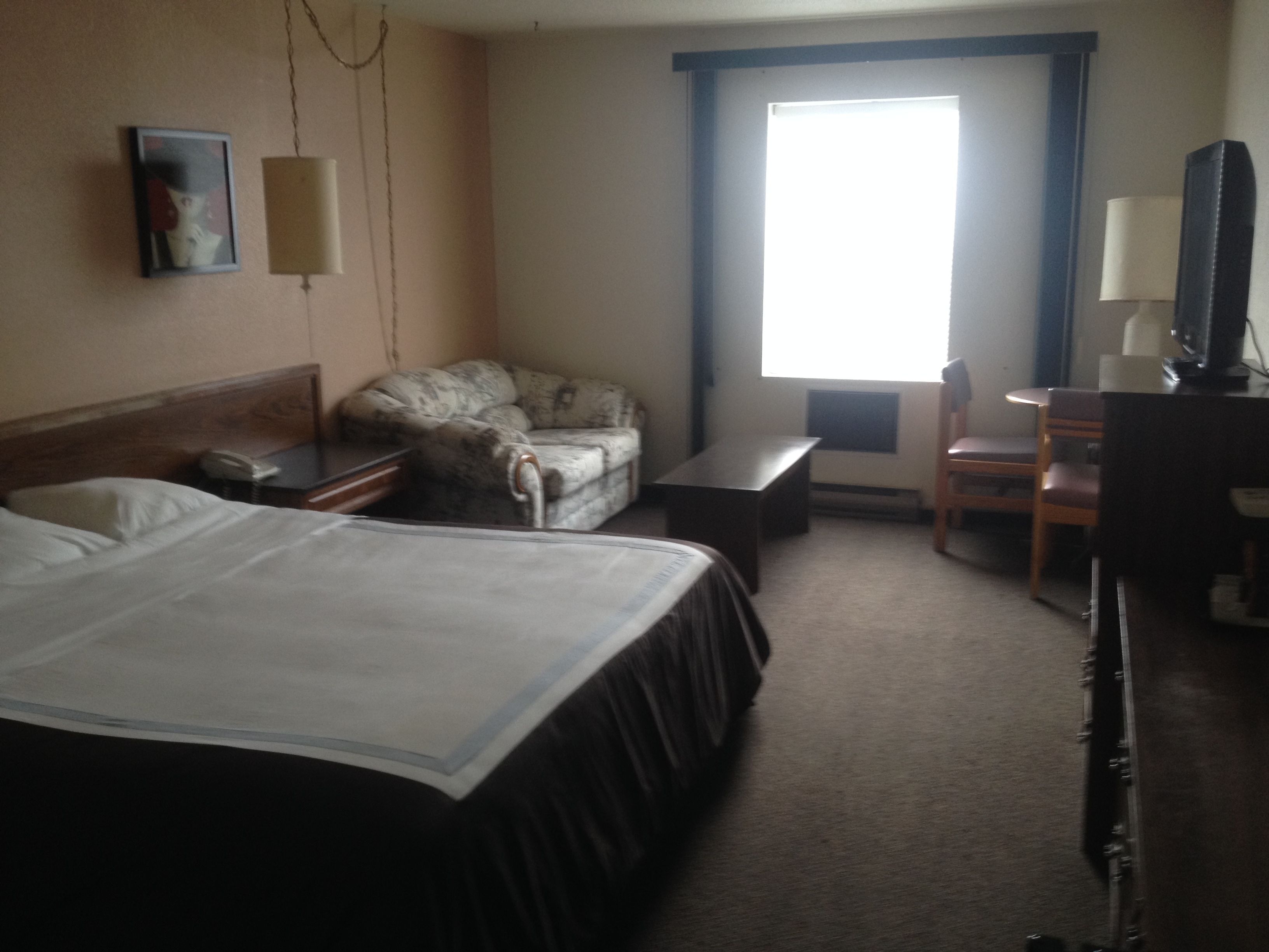 A hotel room with a bed, a chair, a desk, and a television.