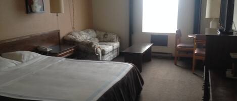 A hotel room with a bed, a chair, a desk, and a television.