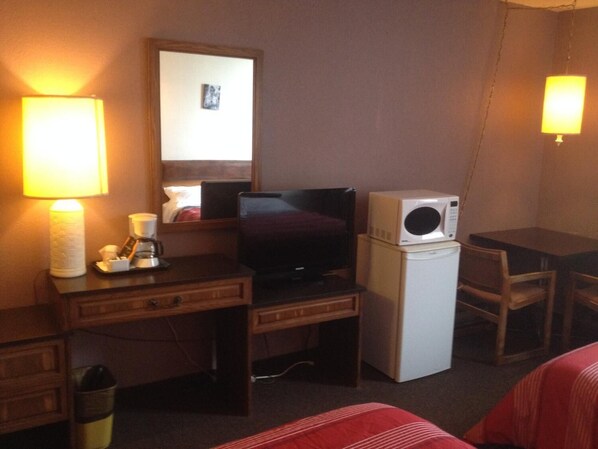 A hotel room with a bed, a desk with a lamp, a television, a microwave, and a small trash bin.