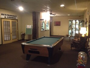 A pool table in a room with a sign for a restaurant and lounge, a chair, and a lamp. - Classic Inn (Melville)