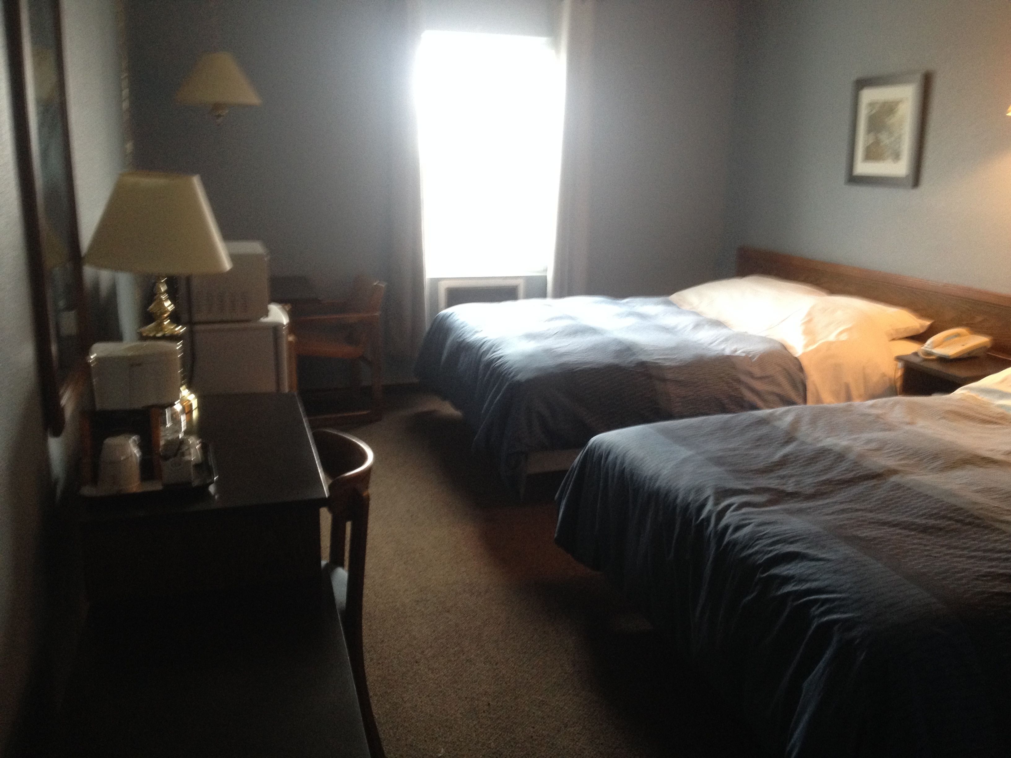 A hotel room with two beds, a desk with a lamp, a chair, and a bedside table with a phone.