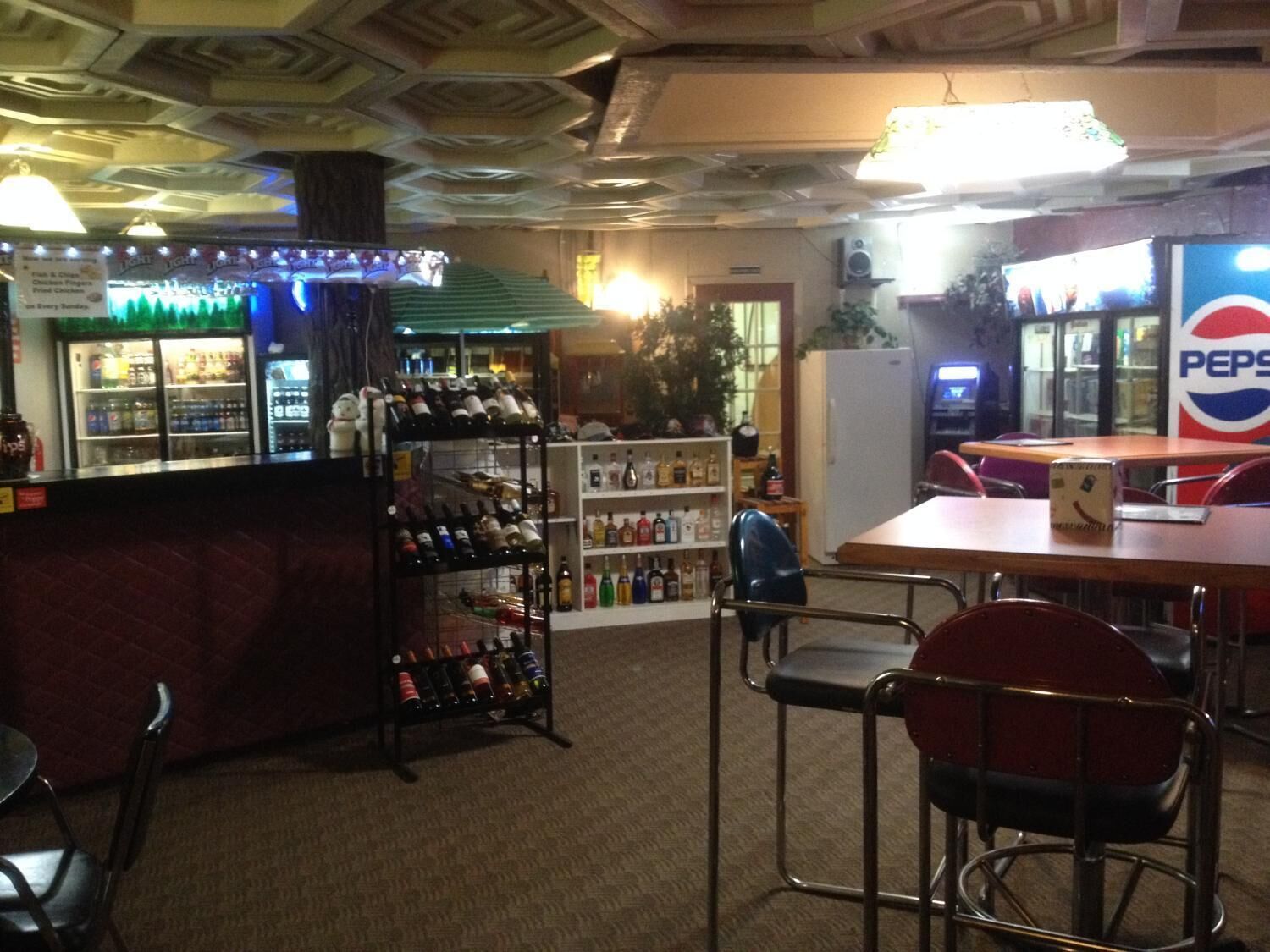 A bar area with a Pepsi sign, shelves of bottles, and a seating area with metal chairs.
