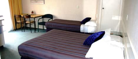 A hotel room with two beds, a desk, chairs, and a small table.