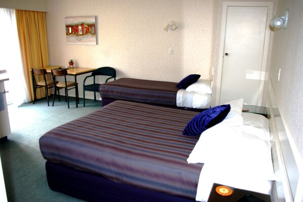 A hotel room with two beds, a desk, chairs, and a small table.