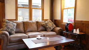 A cozy room with a leather sofa, a wooden coffee table, and a window with a view of a red car outside. - Bliss Lodging (Kutchan)