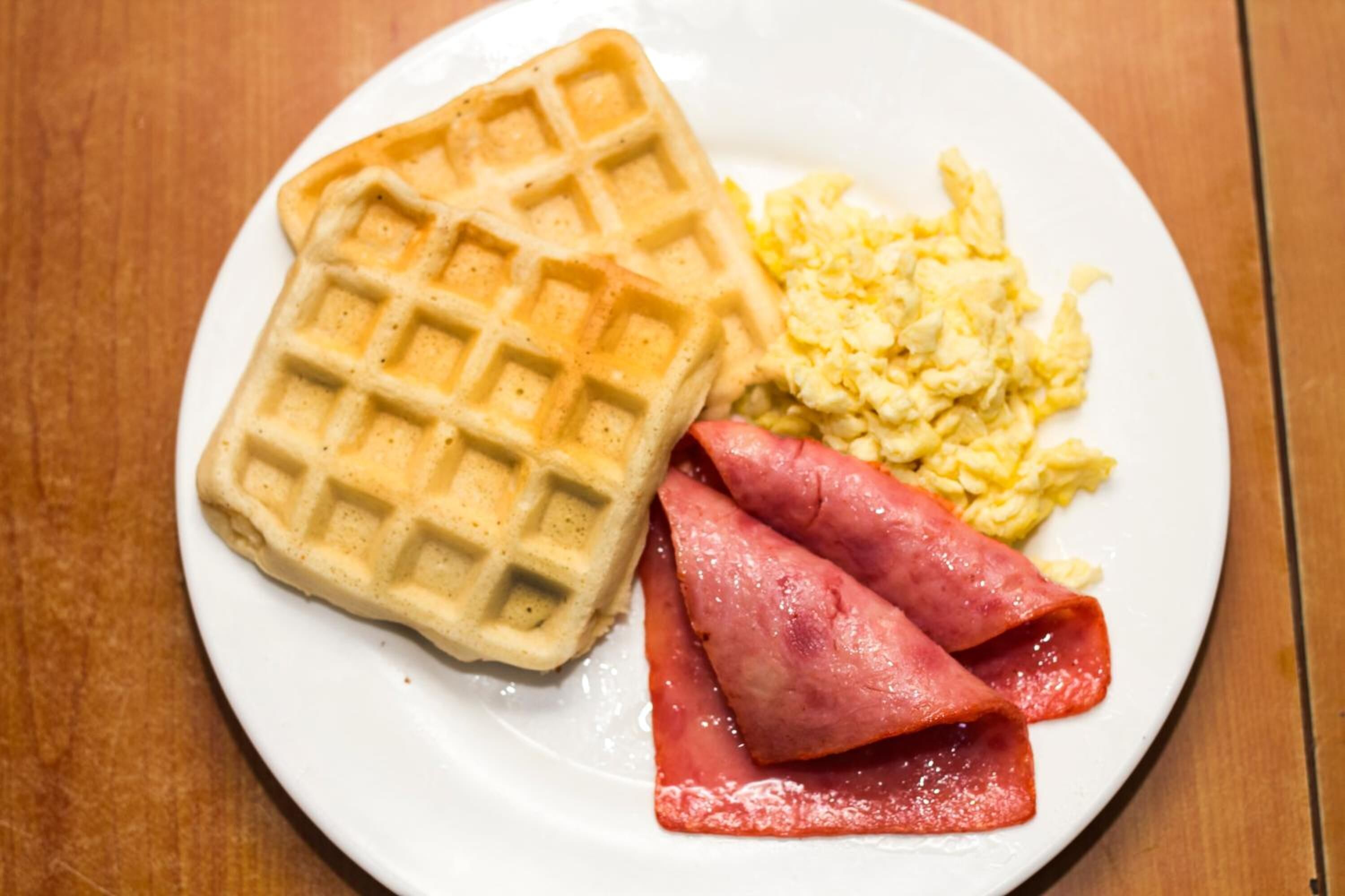 A plate with a waffle, scrambled eggs, and ham slices.
