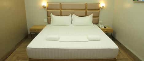 A hotel room with a large bed, headboard with lights, wooden nightstands, and a painting on the wall.