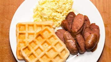 Un plato con huevos revueltos, rebanadas de salchicha y un waffle.