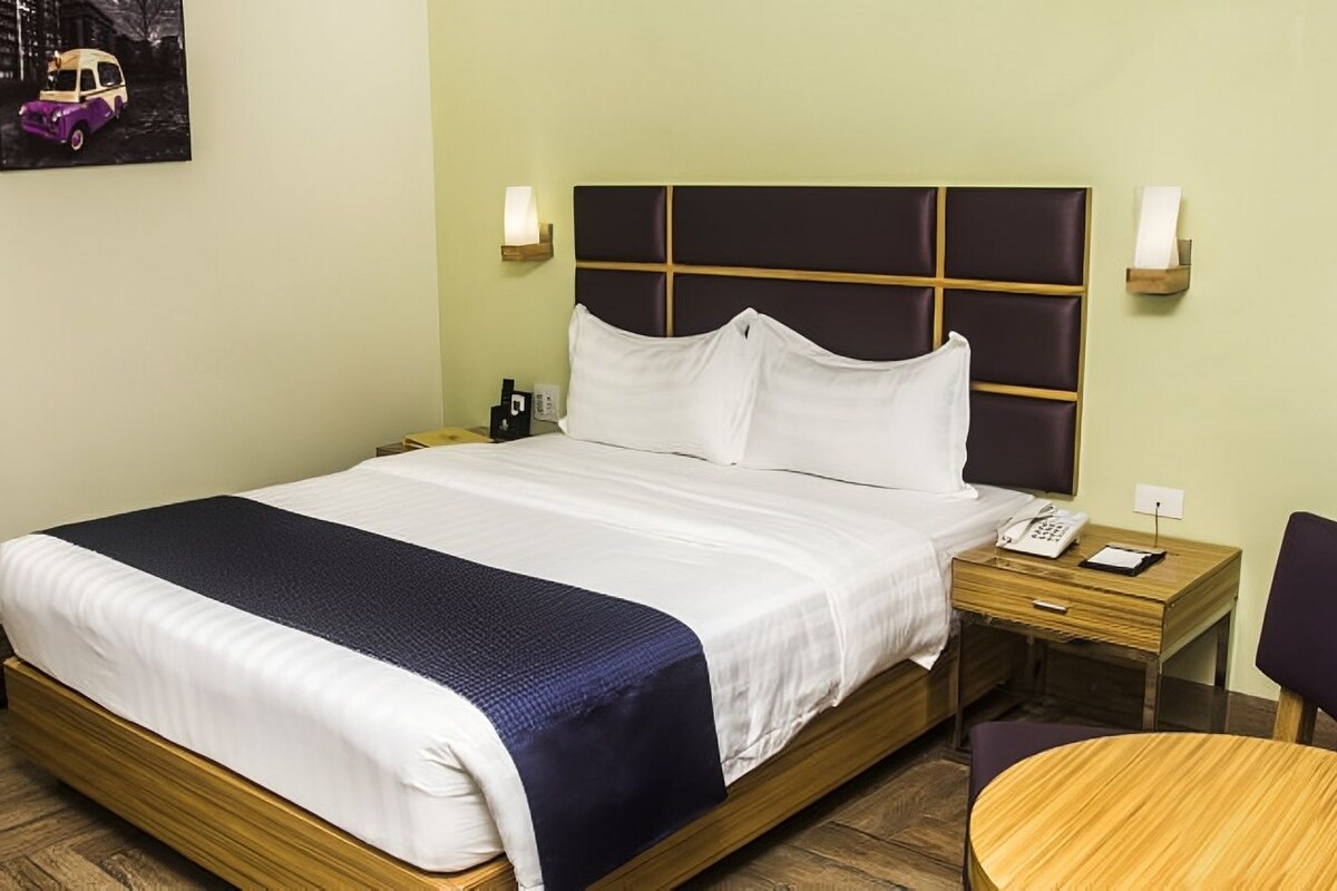 A hotel room with a bed, bedside tables, a chair, and a small table.