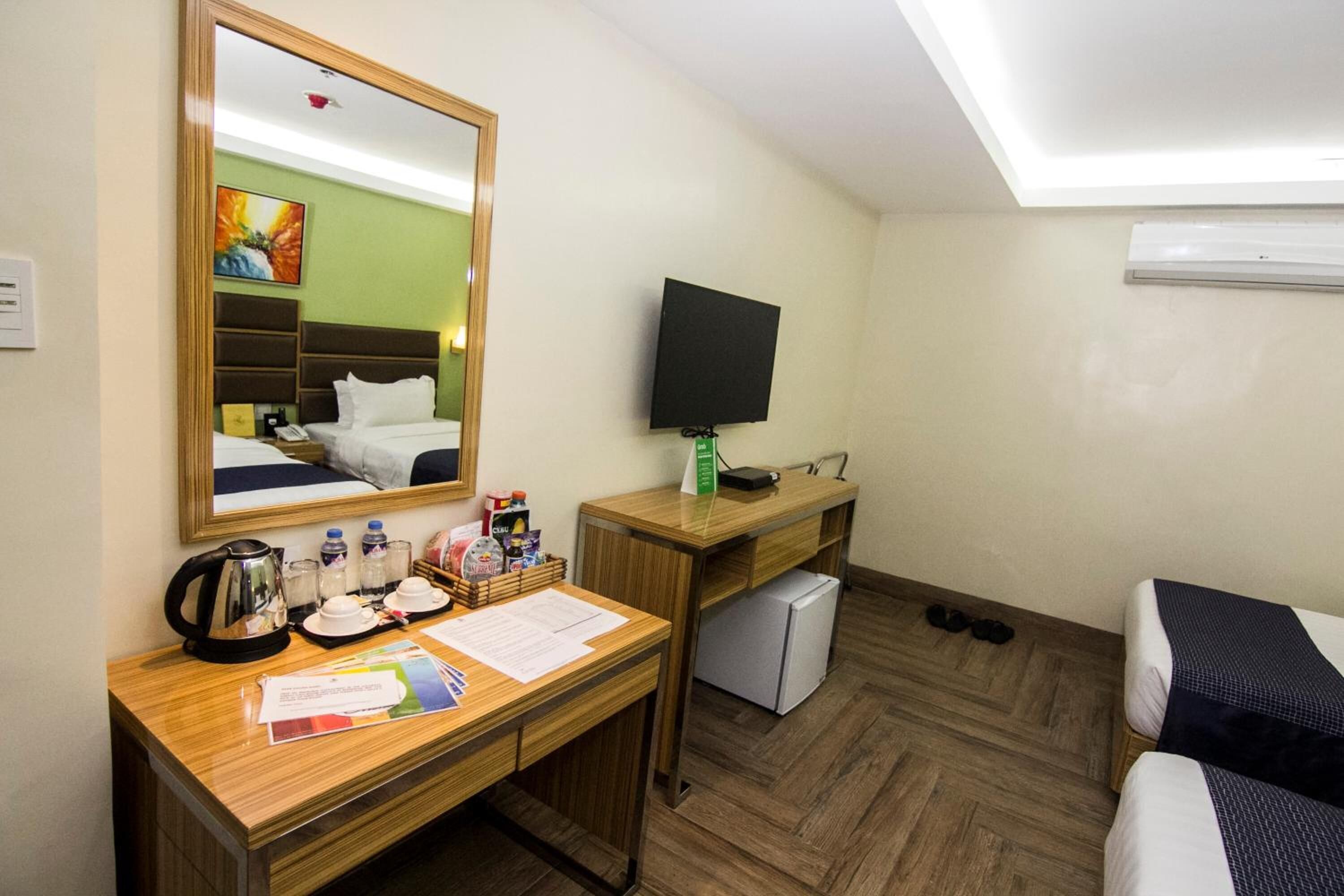 Une chambre d’hôtel avec un bureau en bois, un lit, une télévision et un petit réfrigérateur.