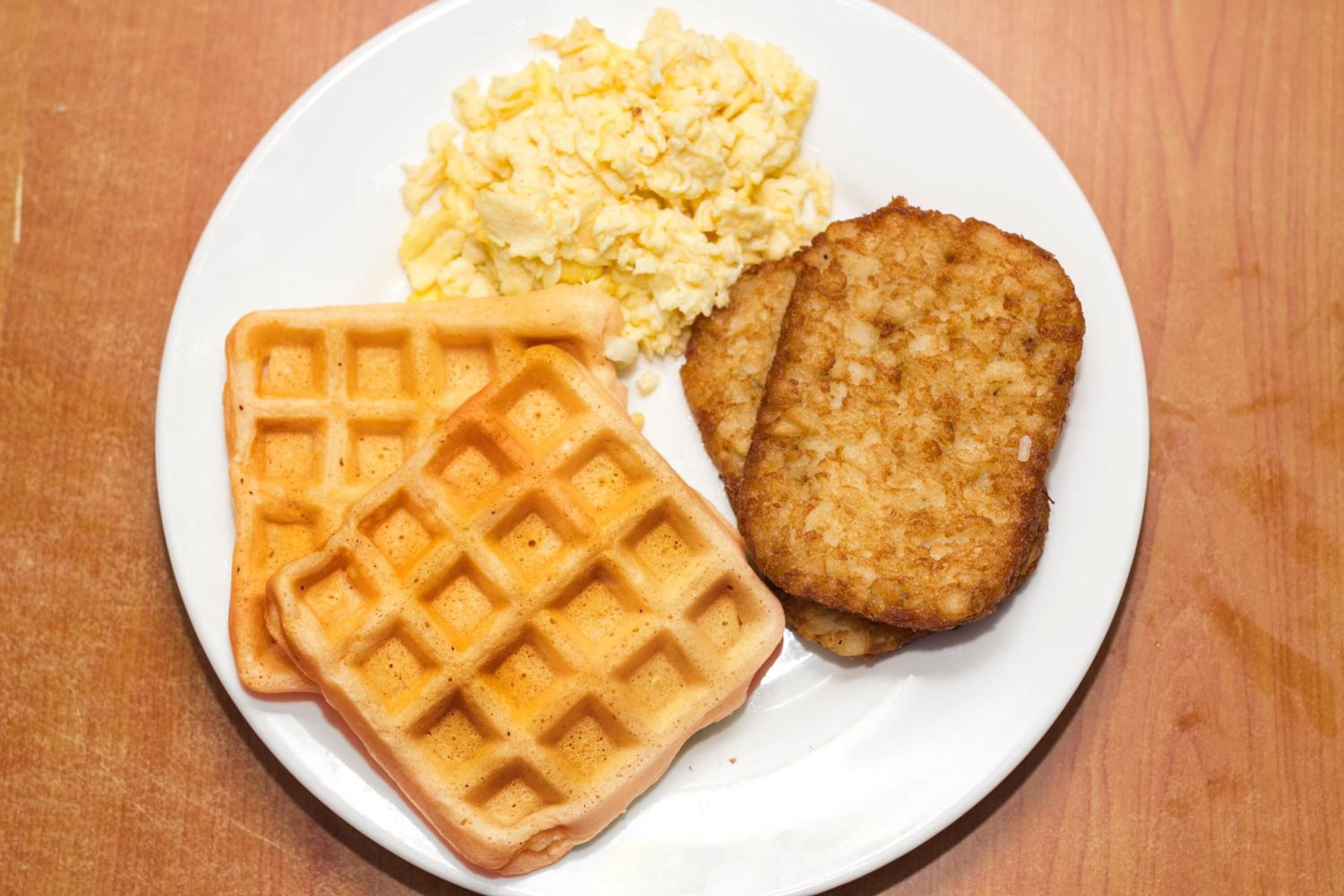 Un plato con un gofre, huevos revueltos y una milanesa frita.