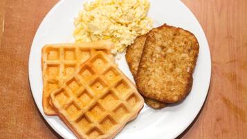 Une assiette avec un gaufre, des œufs brouillés et une escalope panée.