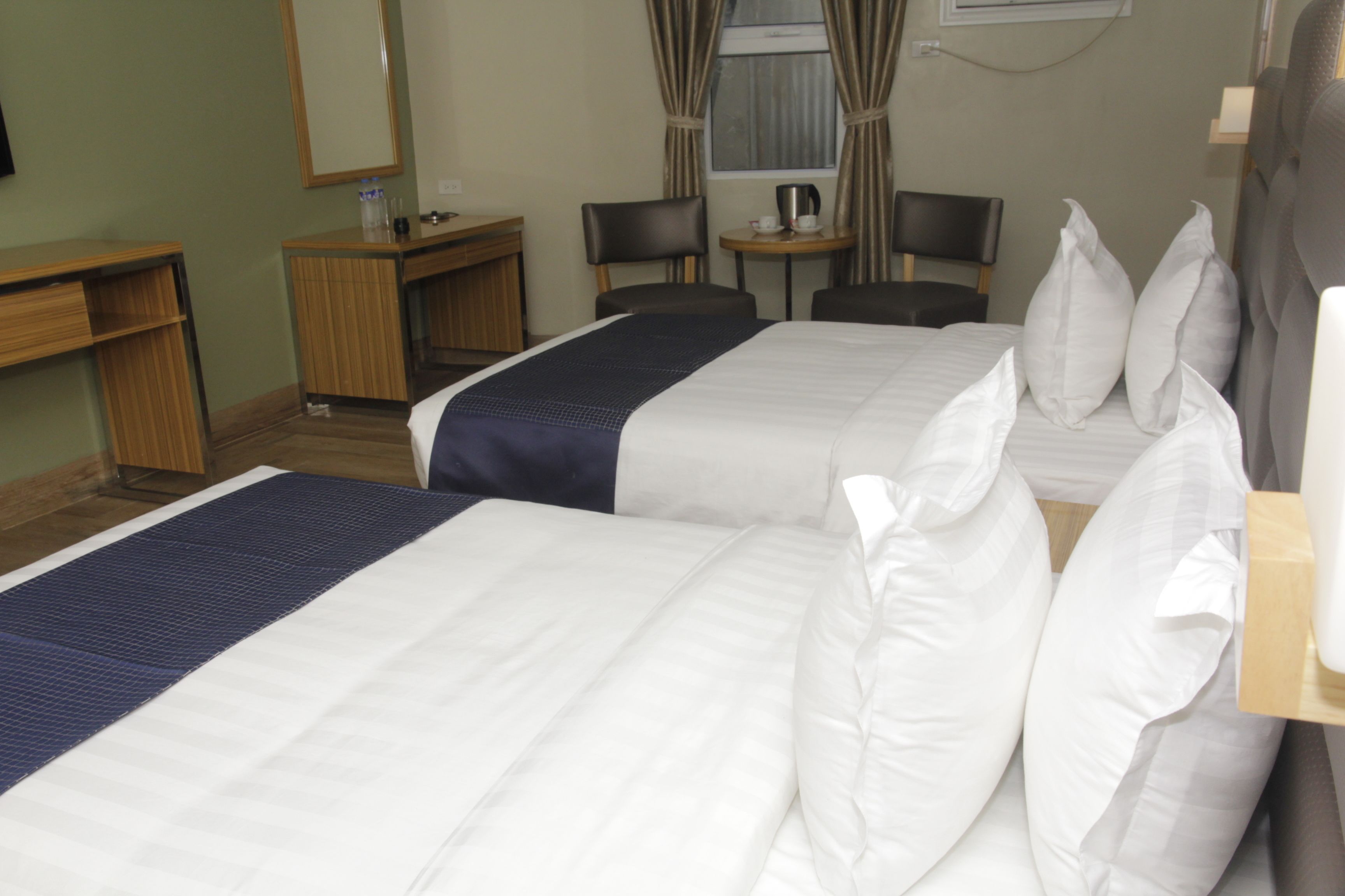 Habitación de hotel con dos camas, un escritorio, una silla, una mesita y una ventana con cortinas.